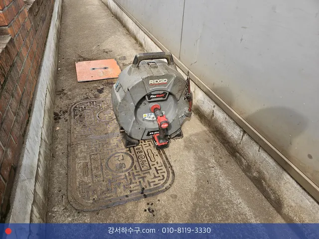좁은 건물 옆 통로 맨홀 옆에 둔 스프링 기계